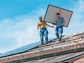 2 Arbeiter tragen ein PV-Modul über ein Hausdach