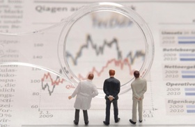 Drei Businessmann Figürchen schauen durch eine Lupe auf eine Börsenchart/ein Diagramm