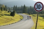 30 km Schild vor grüner Landschaft und kleiner Straße mit Fahrradfahrern