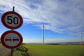 50 und Überholen verboten Schild mit grüner Landschaft und Windrädern im Hintergrund