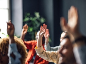 Group of people sitting on a seminar. They have their hand raised.