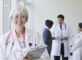Ältere Ärztin mit anderen Ärzten im Hintergrund