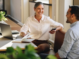 Businesswoman sitting at desk and explaining new project to coworker. Mature woman discussing workin