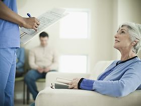 Ältere Dame im Wartezimmer, die mit Pfleger spricht