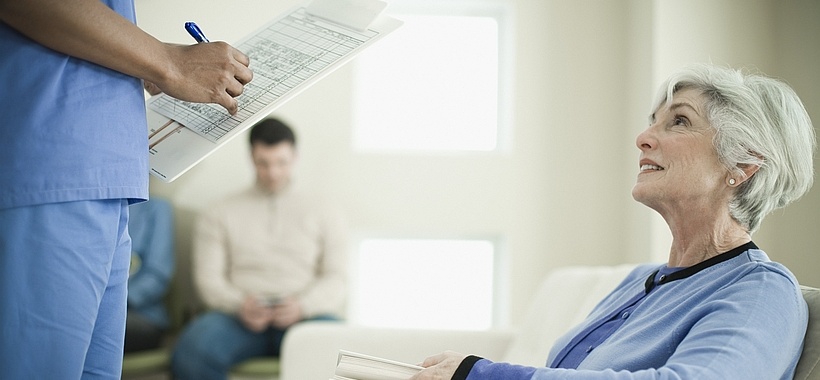 Ältere Dame im Wartezimmer, die mit Pfleger spricht