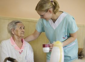 Ältere Frau bekommt Getränk von Pflegeperson