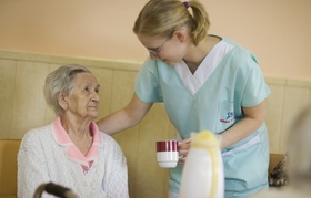 Ältere Frau bekommt Getränk von Pflegeperson