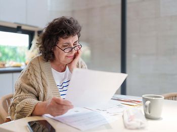 Ältere Frau liest Finanz- oder Steuerunterlagen am Tisch