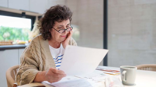 Ältere Frau liest Finanz- oder Steuerunterlagen am Tisch