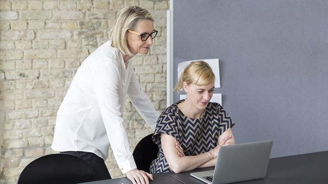 ältere Frau schaut jüngerer Kollegin zufrieden über die Schulter