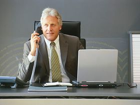 Älterer Manager sitzt am Schreibtisch, telefoniert