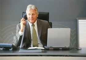 Älterer Manager sitzt am Schreibtisch, telefoniert