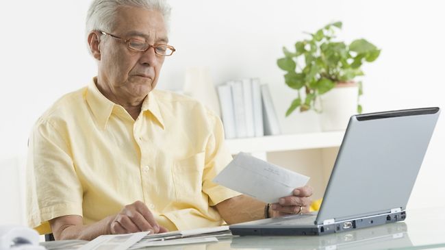 Älterer Mann mit Rechnungen vor Laptop