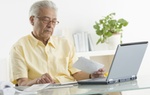 Älterer Mann mit Rechnungen vor Laptop