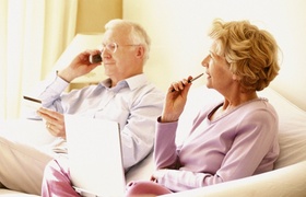 Älteres Ehepaar auf Sofa telefonierend und Notizen machend