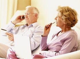 Älteres Ehepaar auf Sofa telefonierend und Notizen machend