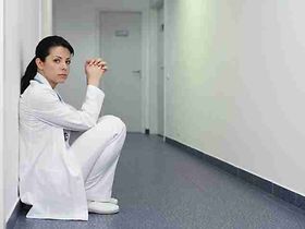 Aerztin hockt an einer Wand im Flur