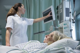 Pflegerin Ärztin schaut auf Bildschirm im Vordergrund alte Frau in Krankenbett