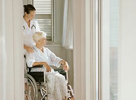 Alte Frau im Rollstuhl betreut von Pflegepersonal