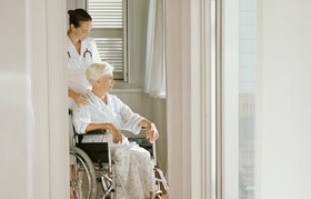 Alte Frau im Rollstuhl betreut von Pflegepersonal