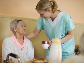 Altenheim, Pflegerin bringt Seniorin eine Tasse