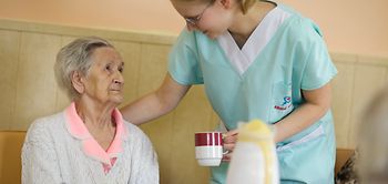 Altenheim, Pflegerin bringt Seniorin eine Tasse