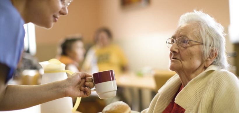 Altenheim, Pflegerin gibt Seniorin eine Tasse und Gebaeck