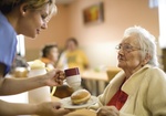 Altenheim, Pflegerin gibt Seniorin eine Tasse und Gebaeck
