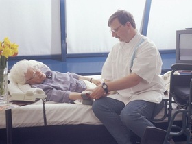 Altenpfleger beim Blutdruckmessen bei aelterer Seniorin am Bett