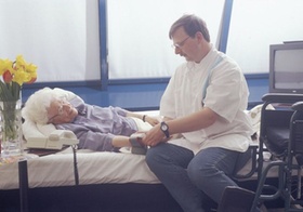Altenpfleger beim Blutdruckmessen bei aelterer Seniorin am Bett