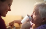Altenpflegerin unterstützt ältere Frau beim Trinken