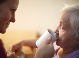 Altenpflegerin unterstützt ältere Frau beim Trinken