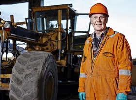 Alter Mann mit Bagger auf Baustelle
