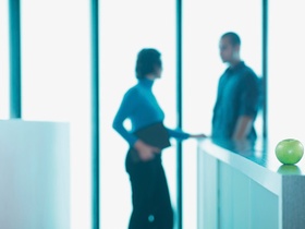 Apfel liegt in Büro, zwei Personen im Hgr.