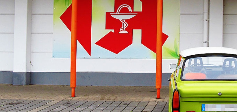 Apothekenzeichen auf Supermarktwand vor Parkplatz