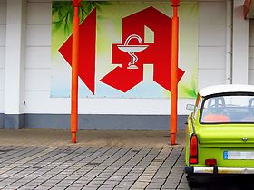 Apothekenzeichen auf Supermarktwand vor Parkplatz