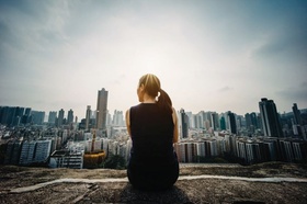 Young woman sitting on the top of mountain enjoying the panoramic view of spectacular city skyline