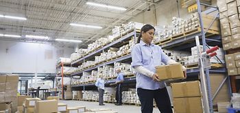 Arbeiterin kontrolliert Paket in Lagerhalle-Regale voller Pakete 