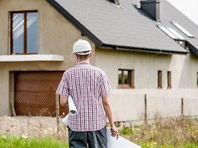 Architekt mit Bauplan unter dem Arm vor Haus
