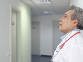 Arzt mit Stethoskop um den Hals lehnt an einer Wand im Flur