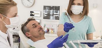 Arzthelferin gibt Zahnärztin eine Spritze Patient liegt auf Stuhl