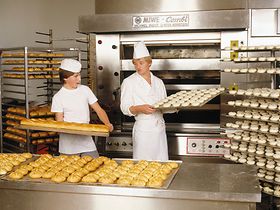 Baecker, Auszubildender, mit Broetchen an Backofen