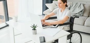 woman in a wheelchair works on the laptop PC in the home office 