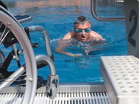 Behindertensport, Mann schwimmt im Schwimmbecken, Rollstuhl steht