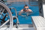 Behindertensport, Mann schwimmt im Schwimmbecken, Rollstuhl steht am Rand