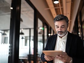 Mature businessman walking and using digital tablet at corridor o