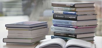 Bücher stapeln sich, ein Buch ist aufgeschlagen