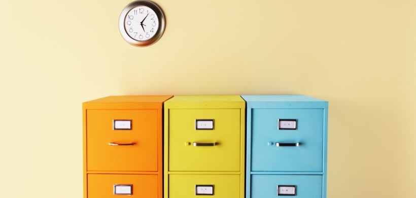 Bunter Aktenschrank vor organgener Wand mit Uhr