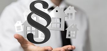 Businessman hält Paragraphenzeichen und Häusersymbol in der Hand