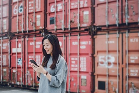 Young business woman using smartphone in industrial container yard
